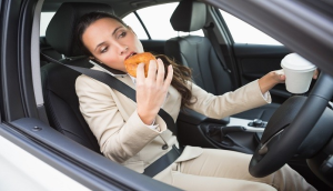 A woman sitting in a car, enjoying a donut with a smile on her face