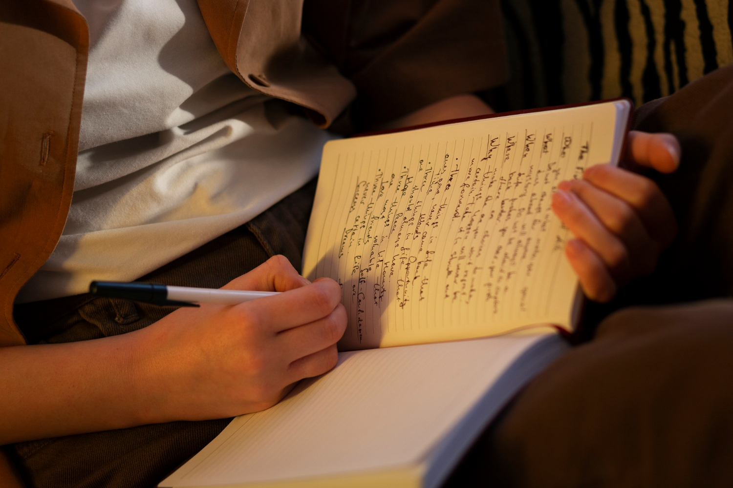 A person writes in a notebook with a pen, focused on their task in a well-lit environment