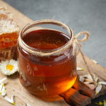 Jar of golden honey with honeycomb and flowers on a rustic wooden board, ideal for natural food and health themes