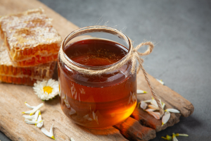 Jar of golden honey with honeycomb and flowers on a rustic wooden board, ideal for natural food and health themes