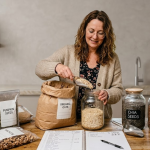Woman preparing organic oats in a kitchen with jars of chia seeds, flax seeds, and mixed nuts on the counter