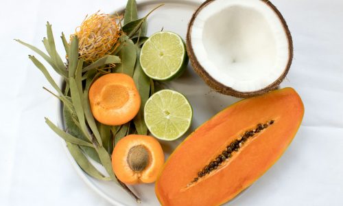 Tropical fruit platter with papaya, coconut, lime, and apricot on a white plate with leafy greens for garnish